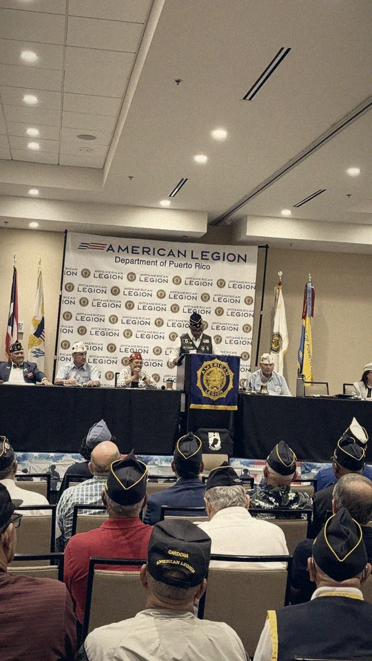 The convention room: the head table, veterans in American Legion caps, and the flags of Puerto Rico and the U.S. Virgin Islands